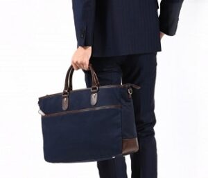 ネイビーのスーツを着て、就活にふさわしいファスナー付きの黒いトートバッグを手に持つ男性の背面