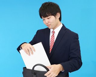 通勤バッグにA4書類を入れるスーツ姿の男性