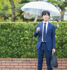 雨の日に傘を差し、黒い就活トートバッグを持って移動するリクルートスーツ姿の男性