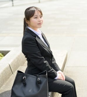 スーツを着て黒のトートバッグを隣に置く女子就活生の姿