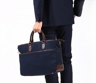 ネイビーのスーツを着て、就活にふさわしいファスナー付きの黒いトートバッグを手に持つ男性の背面